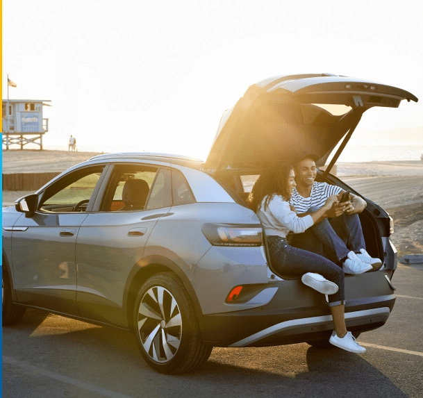 Couple sitting in the open trunk of their SUV reviewing their auto insurance options
