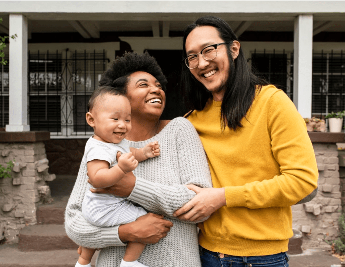 image of a young couple laughing in front of their home while holding their young child