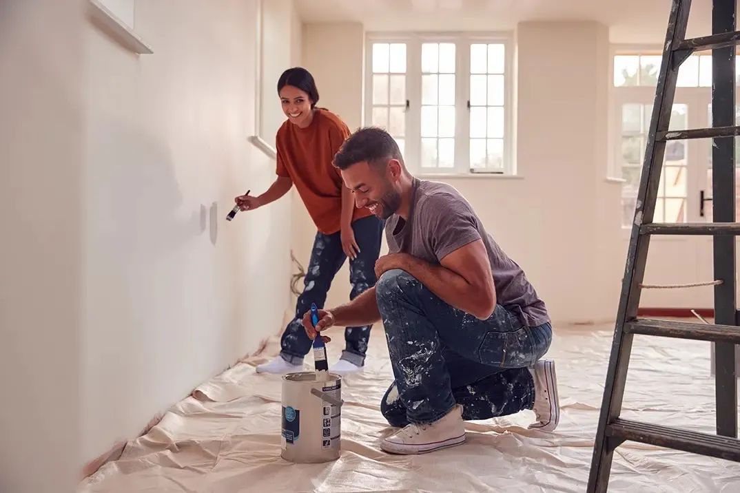 A happy young couple are painting the interior walls of their new home, now that they are protected by Mortgage Protection Insurance.