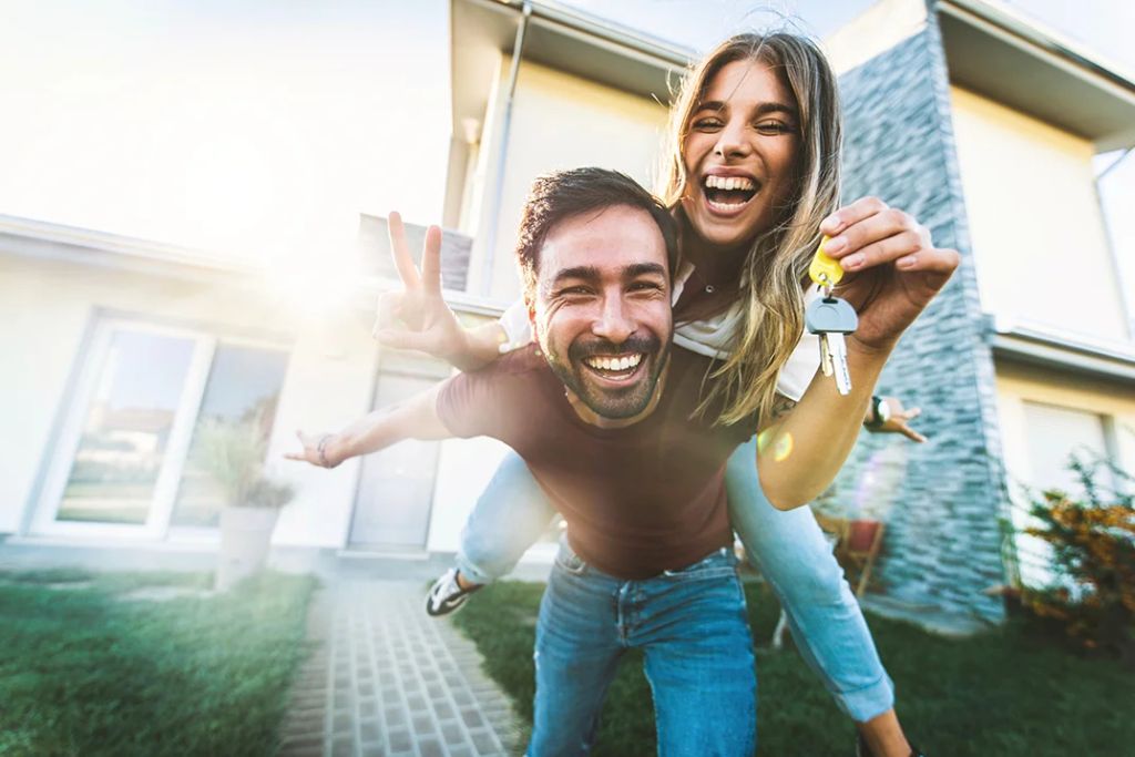 A couple poses happily in front of their new home protected by Mortgage Protection Insurance.