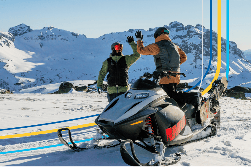 two people high-five beside a snowmobile