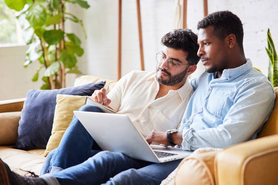 Two men looking at laptop and making notes on a paper.