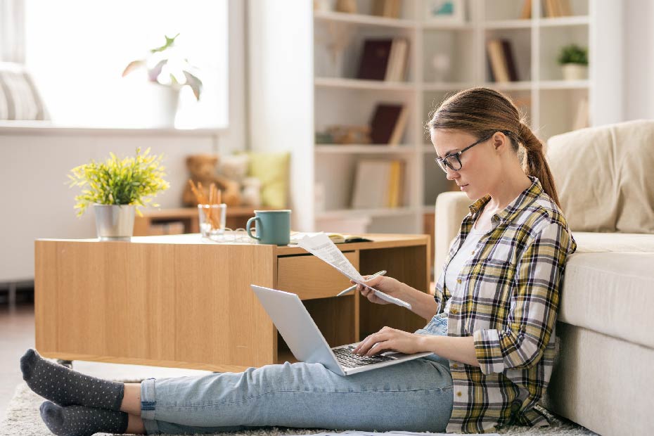 A woman looking at laptop screen and holding paper.