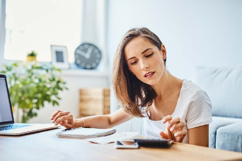 A woman looking at bills and doing calculation on a calculator.