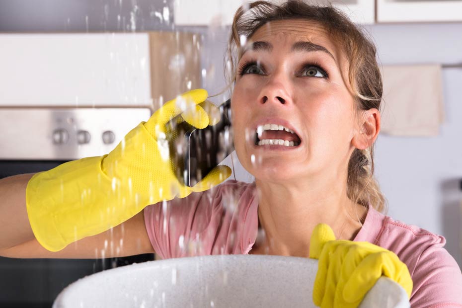 Distressed woman on phone holding a bucket to prevent water leakage