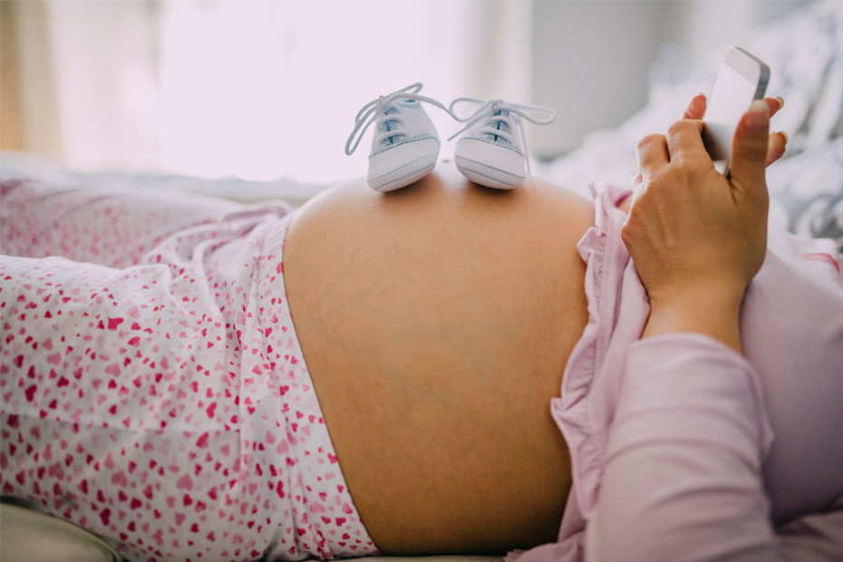 Pregnant woman on her phone, and thinking about how to prepare for the arrival of the baby.