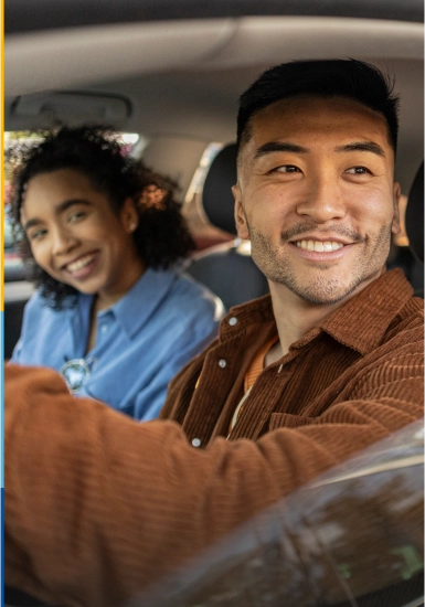 Couple smiling looking out the window of car, covered by personal vehicle insurance