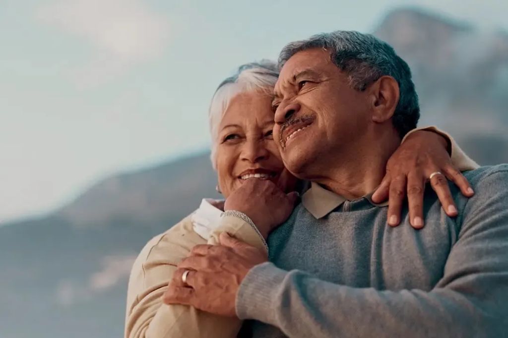 Un couple de personnes âgées (un homme et une femme) regarde le coucher du soleil en s'étreignant, maintenant qu'ils sont protégés par une assurance-vie.