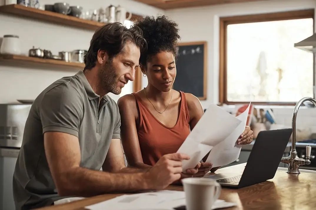 Un couple, un homme blanc et une femme noire, examine des documents hypothécaires sur leur plan de travail de cuisine, alors qu'ils apprennent ce qui influence leurs primes d'assurance-vie.