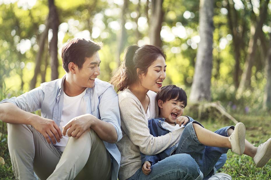 Couple et leur enfant assis et souriant dans un parc