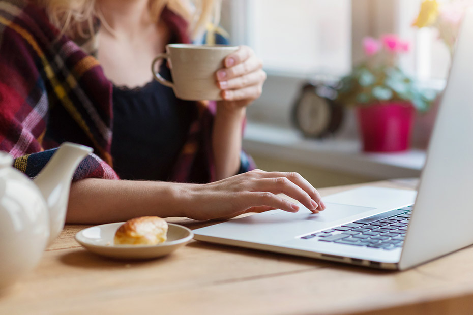 Femme buvant du café tout en vérifiant son portefeuille REER sur un ordinateur